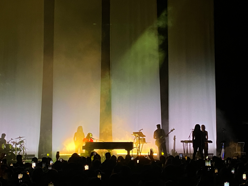 Marina and the Diamonds performs at the Masonic auditorium. Marina sits at a grand piano, other band members are silhouetted.