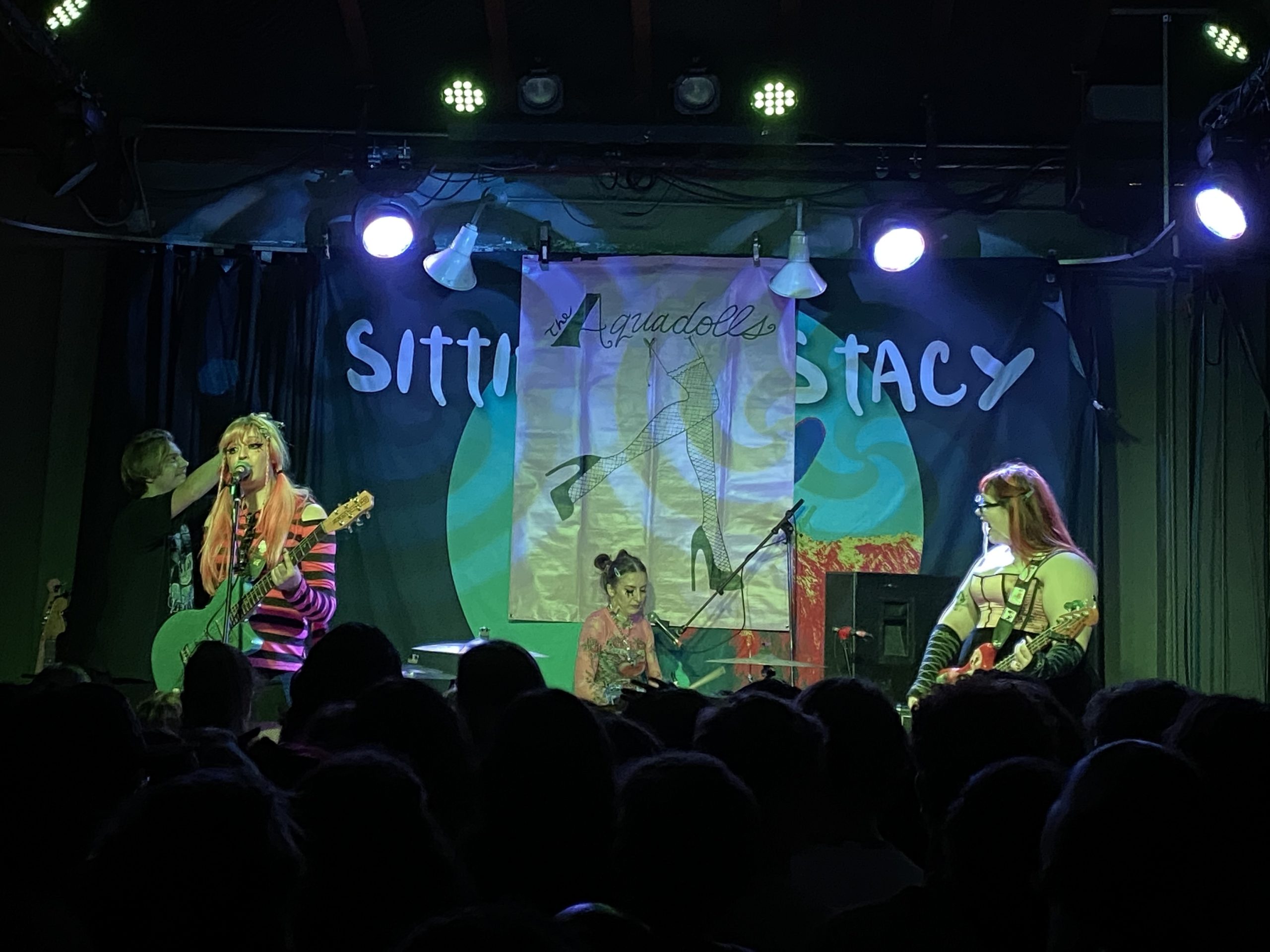 The Aquadolls, a rock band, performs at the Catalyst Atrium. The three performers have expressive outfits.